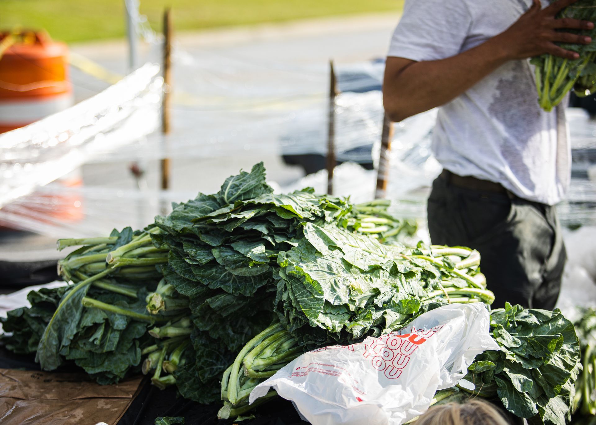 A man is standing next to a pile of green vegetables.