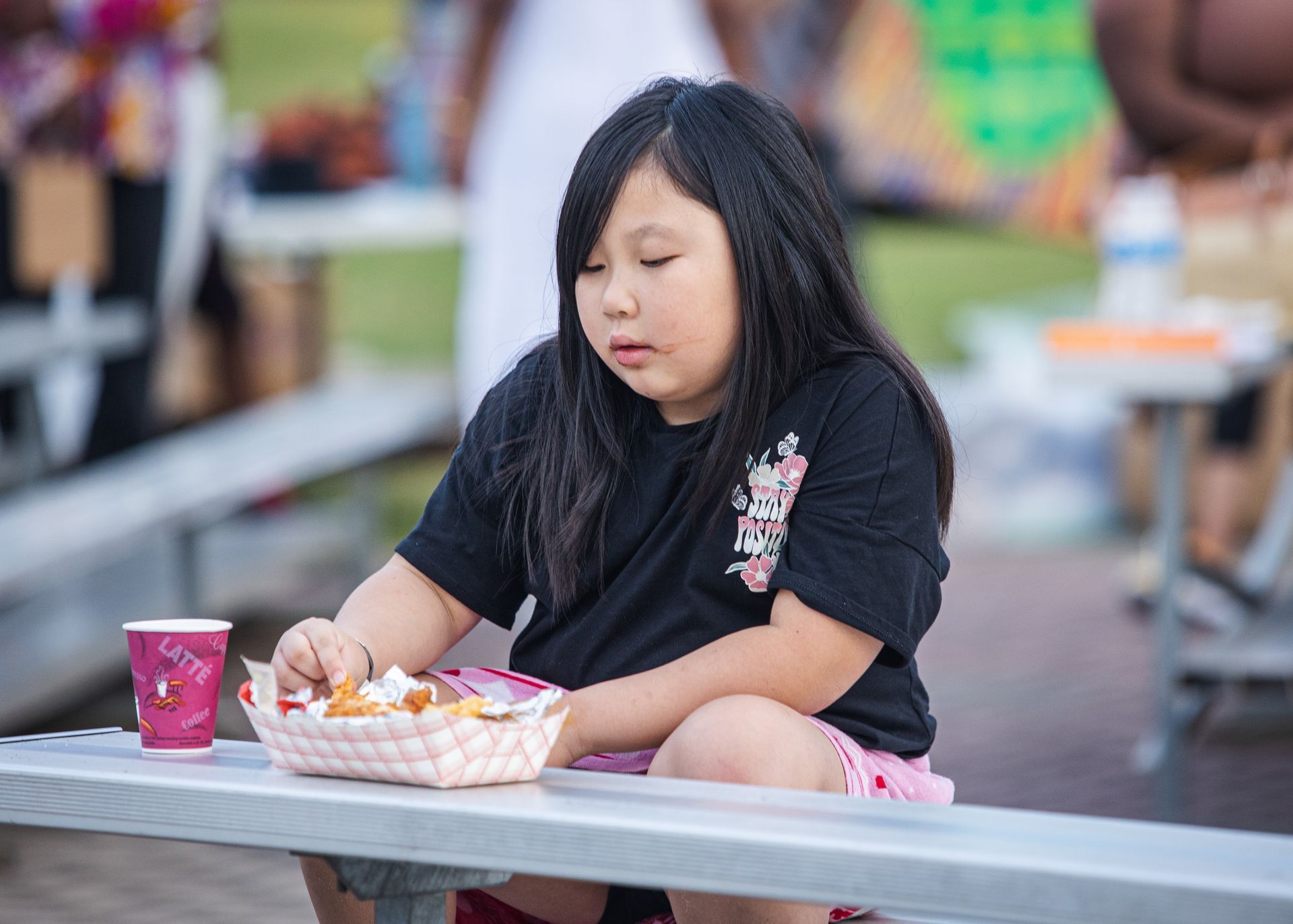 A little girl is sitting on a bench eating french fries.