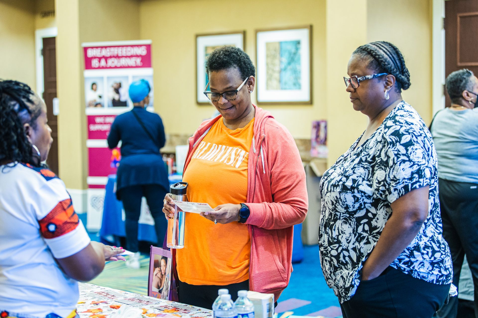 A group of women are standing around a table talking to each other.