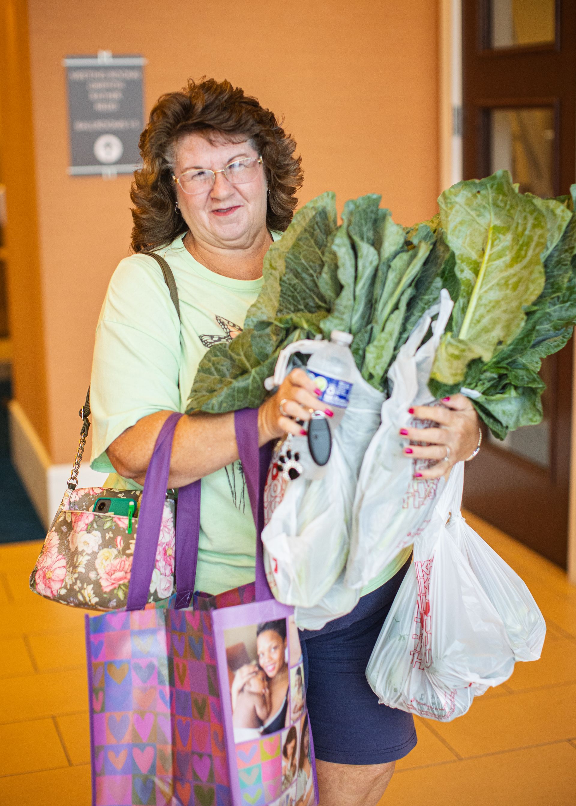 A woman is carrying a bag of lettuce and a bottle of water.