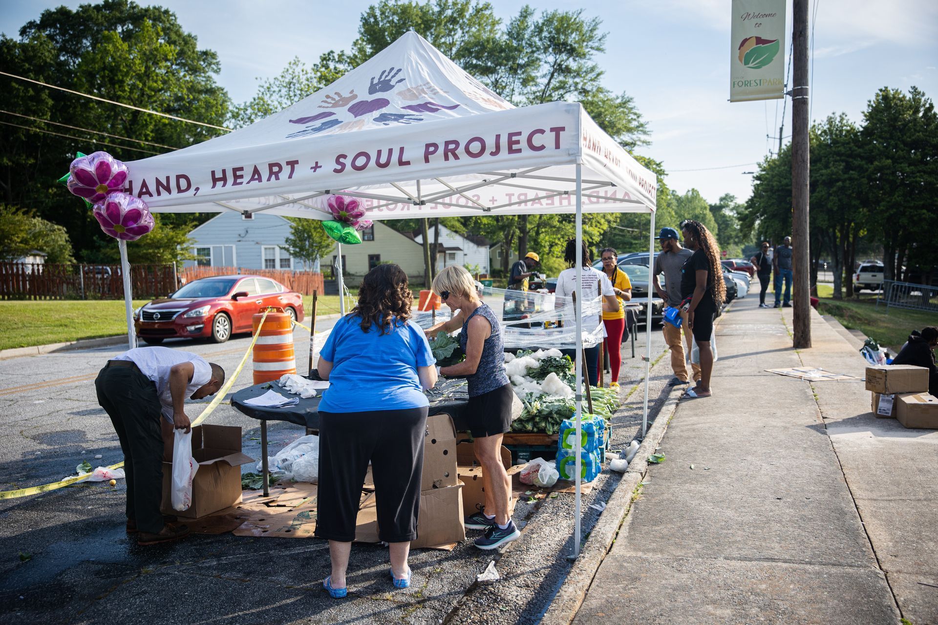 A group of people are standing under a tent that says hand heart soul project.