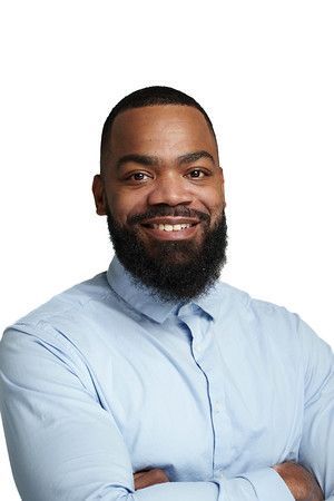 A man with a beard and a blue shirt is smiling with his arms crossed.
