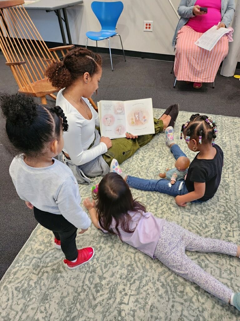 A group of young girls are sitting on the floor reading a book.