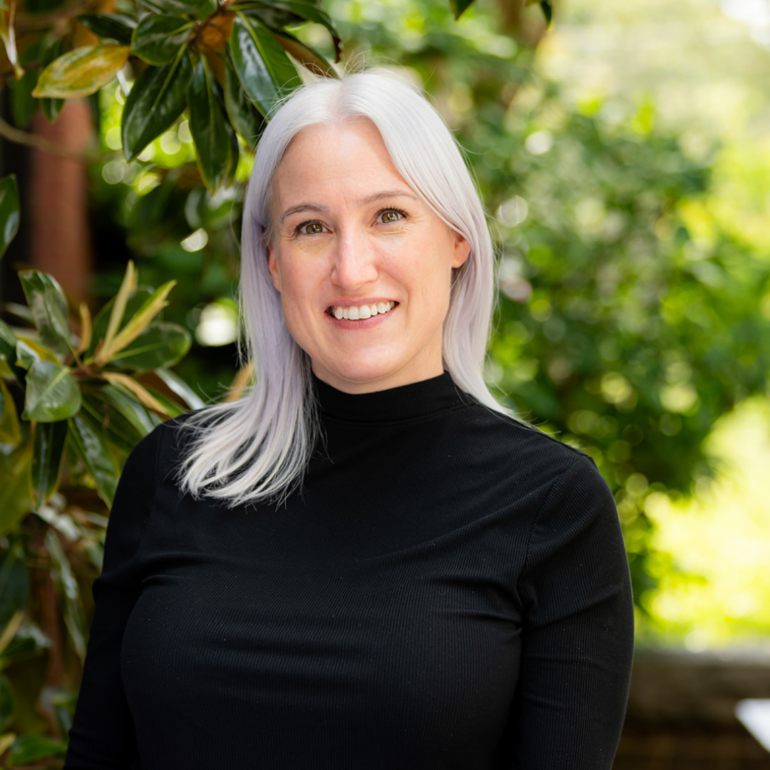 A woman with white hair is wearing a black shirt and smiling.