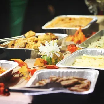 A table topped with trays of food and a flower.
