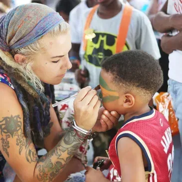 A woman is painting a child 's face with green paint
