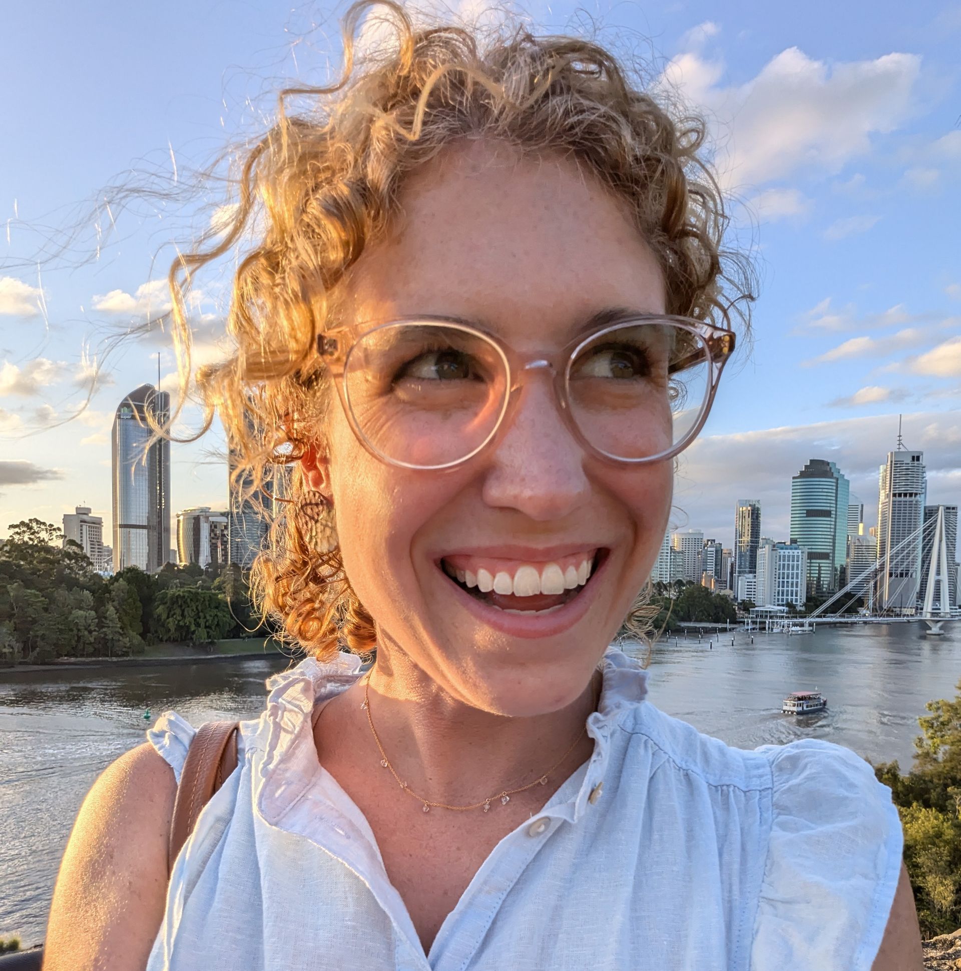A woman wearing glasses is smiling in front of a city skyline.