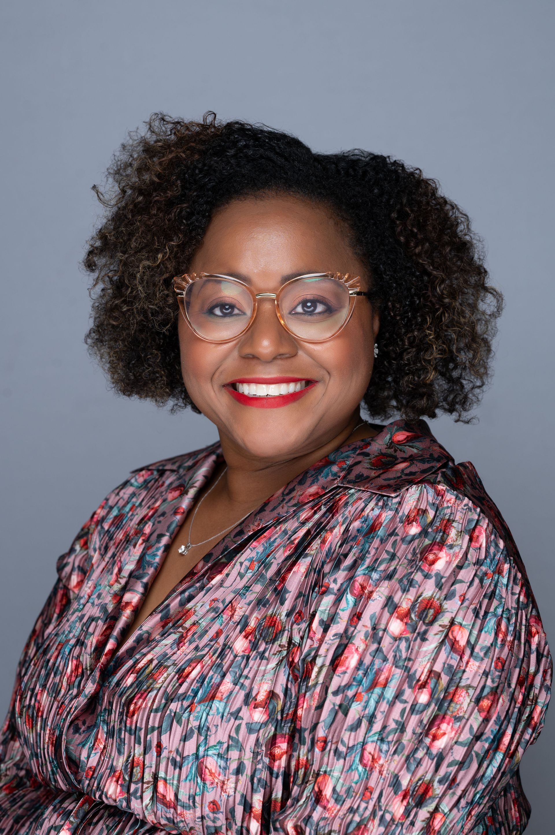 A woman wearing glasses and a floral shirt is smiling for the camera.