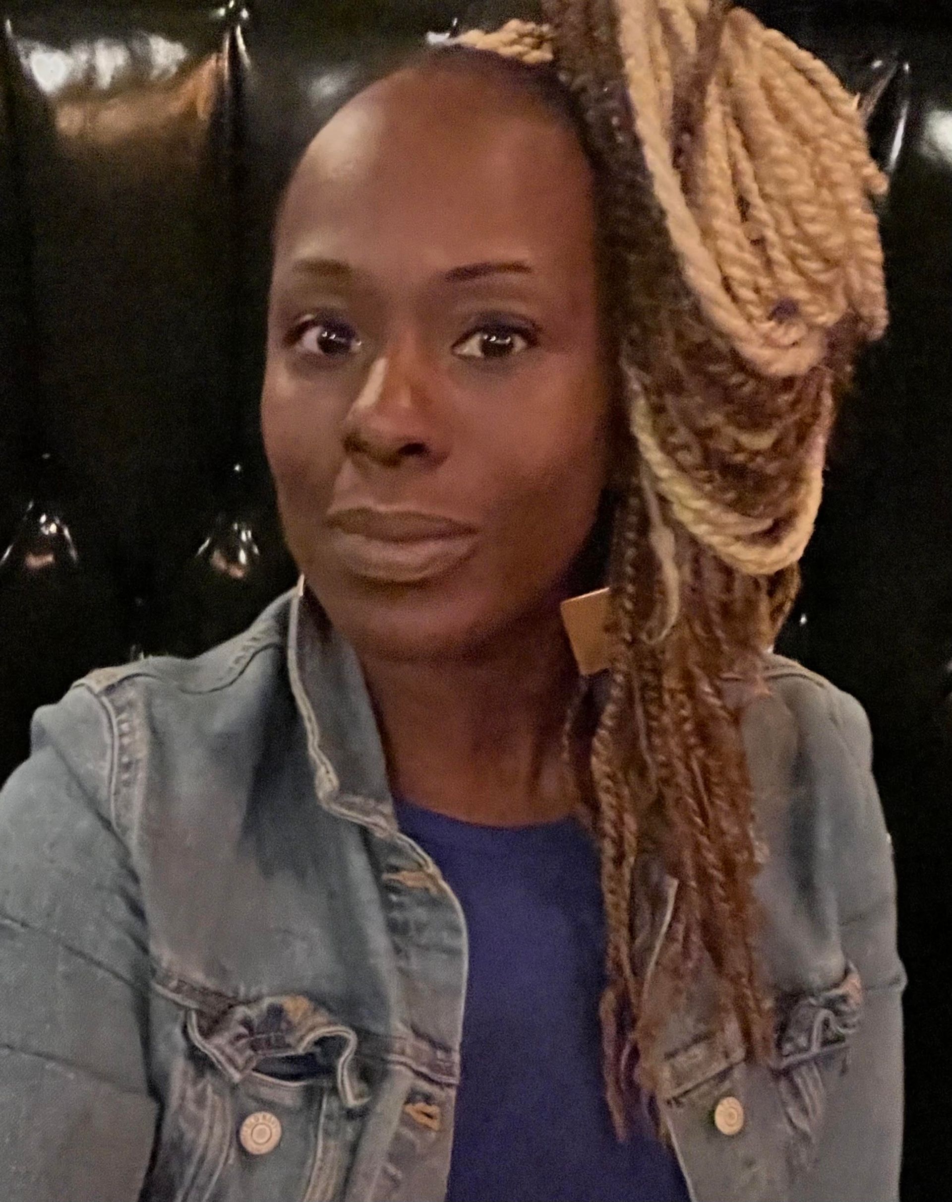 A woman with braids is wearing a blue shirt and a denim jacket.