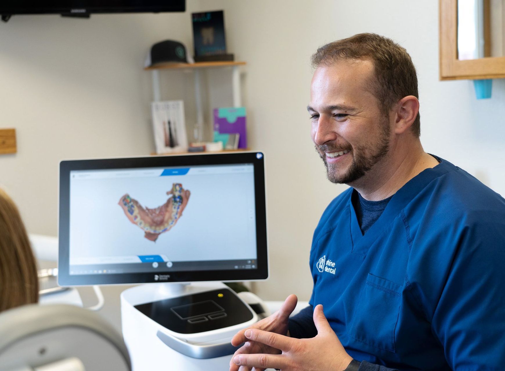 A man in a blue scrub is sitting in front of a computer screen.