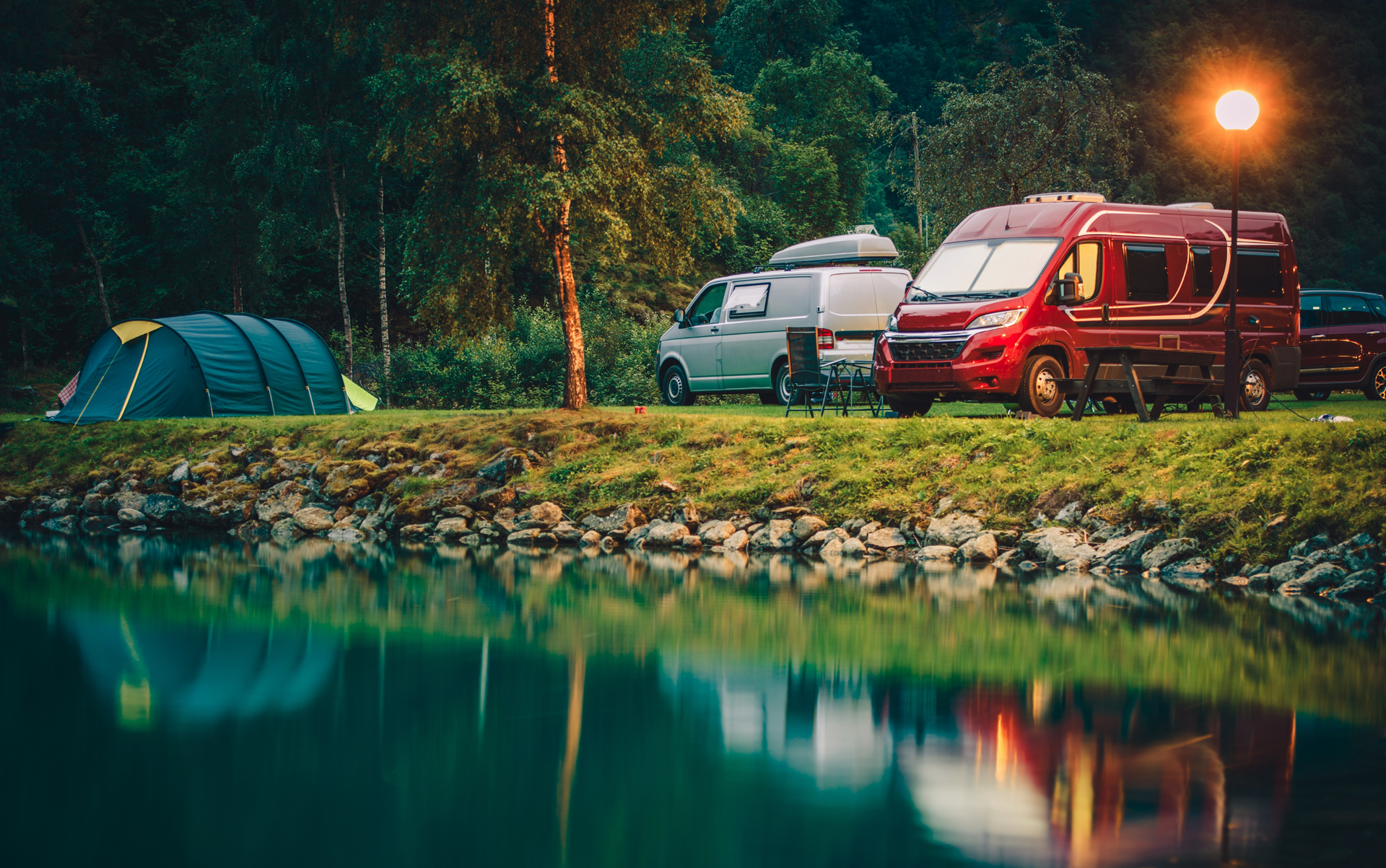 Camping scene: Tent, campervans, and water, with a sunlit sky.