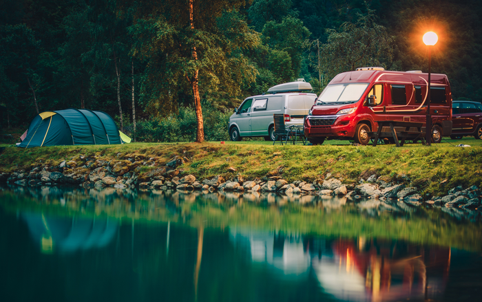 Camping scene: Tent, campervans, and water, with a sunlit sky.