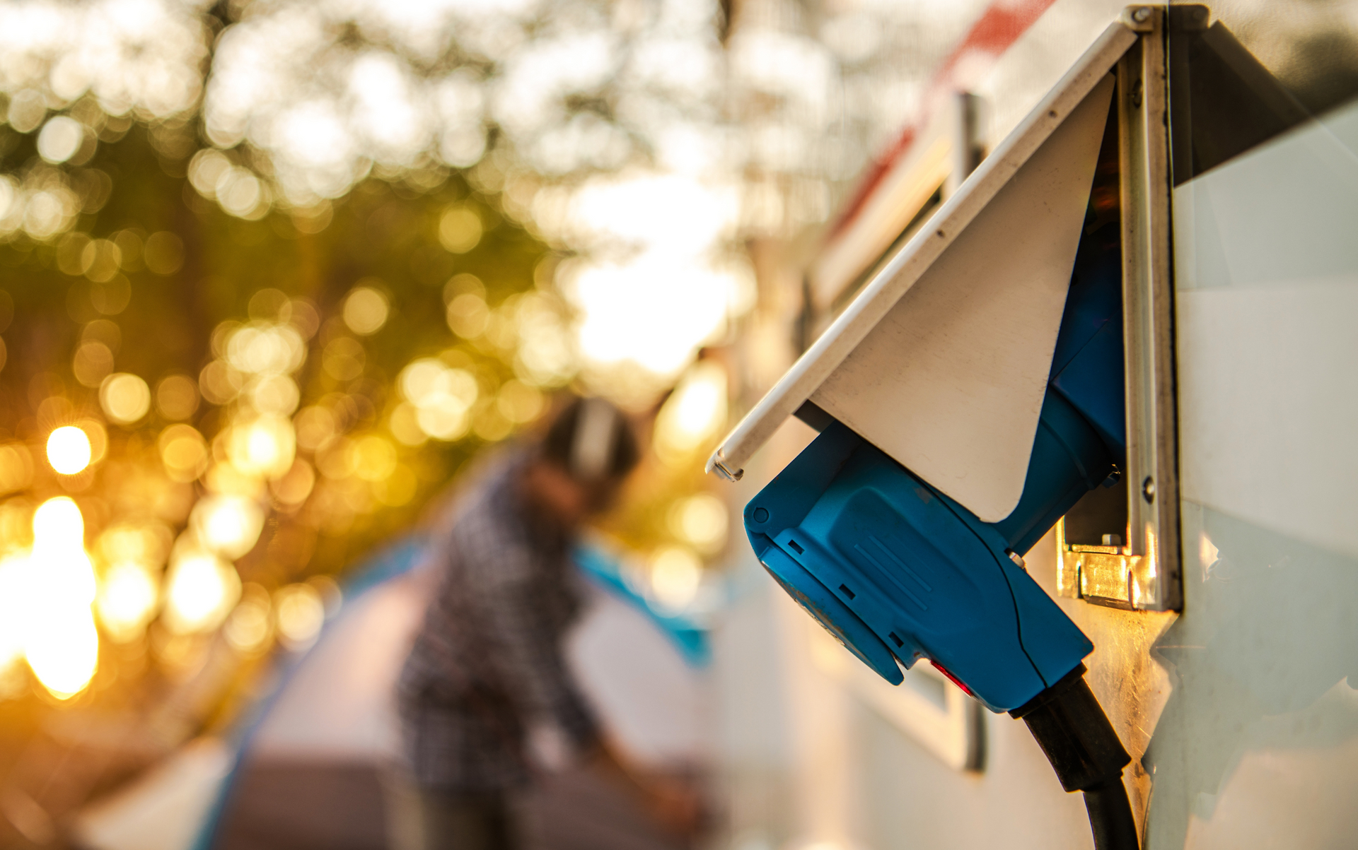 Blue EV charger plugged into a vehicle in a sunlit outdoor setting.