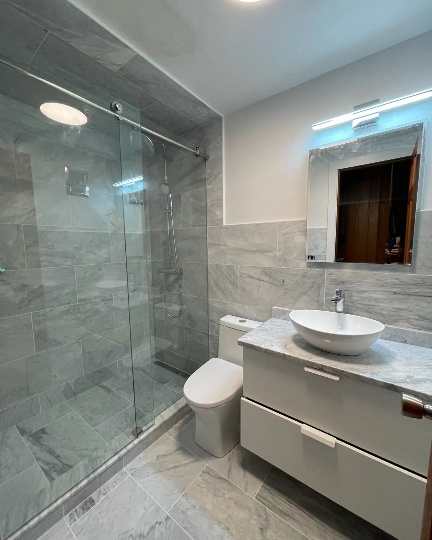 A bathroom with a toilet , sink , mirror and walk in shower.