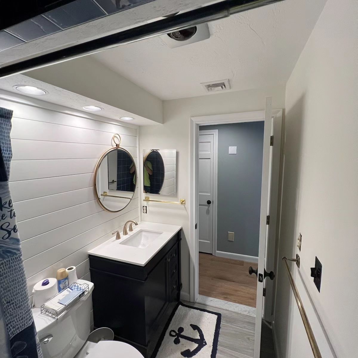 A bathroom with a toilet , sink , mirror and anchor rug.