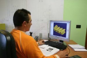 un uomo alla scrivania che osserva il monitor di in computer con un disegno tecnico