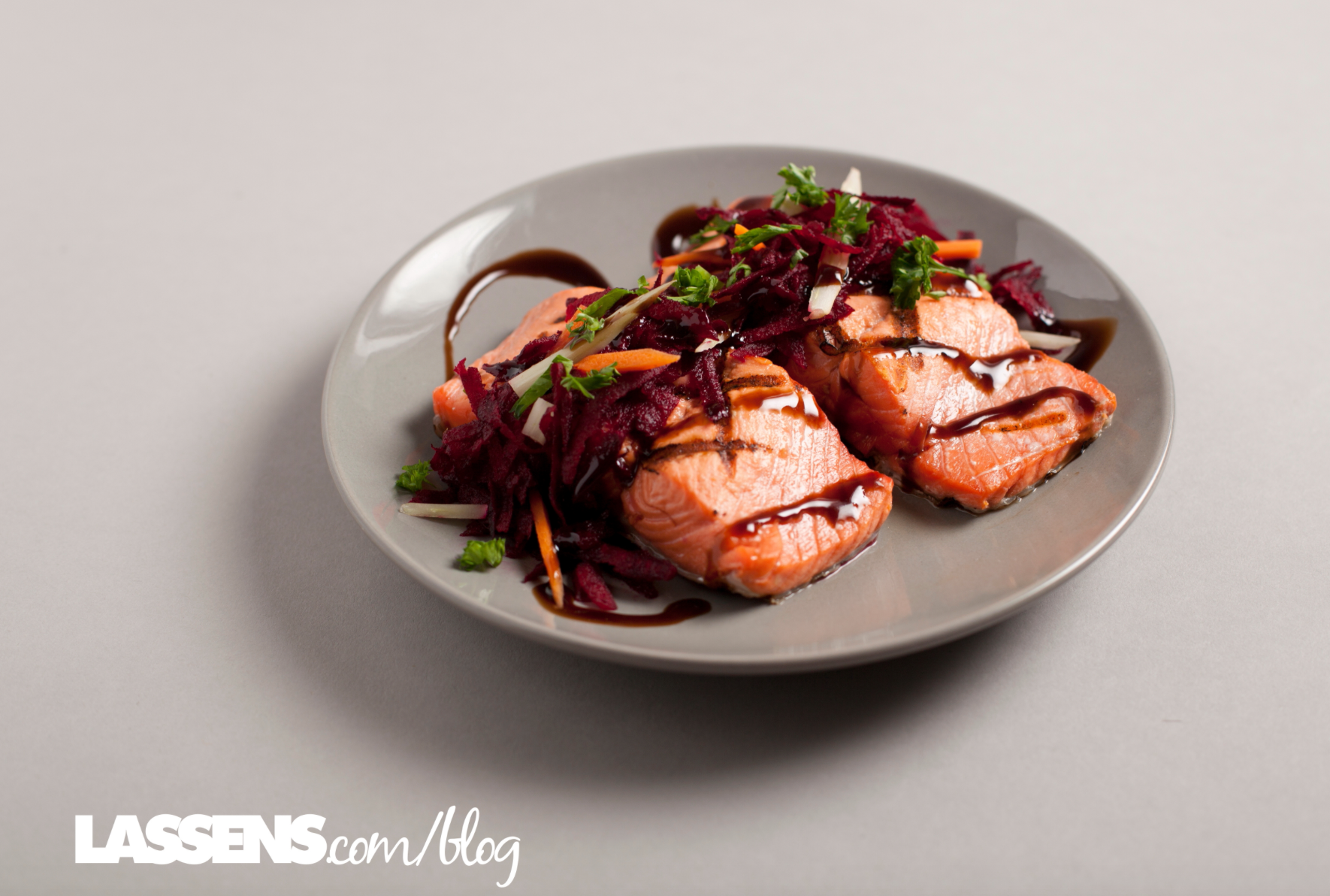 Cooked salmon fillets with shredded beets, carrots, and balsamic glaze on a gray plate.