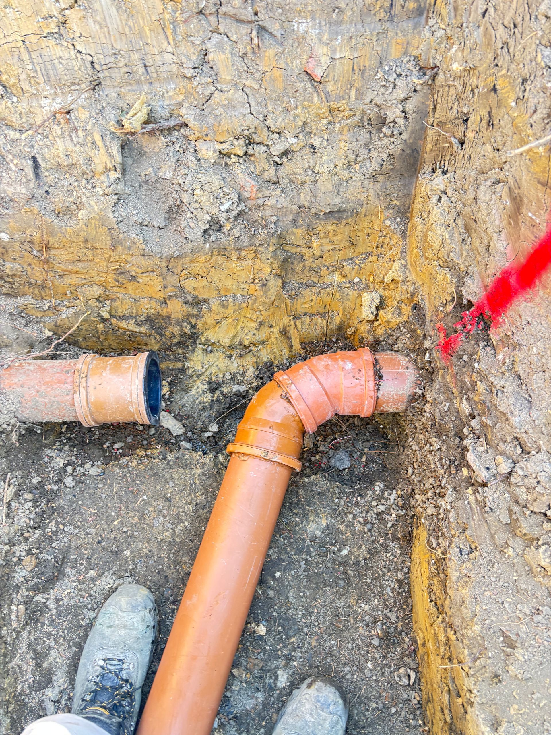 Construction workers in orange vests installing large metal pipes in a trench