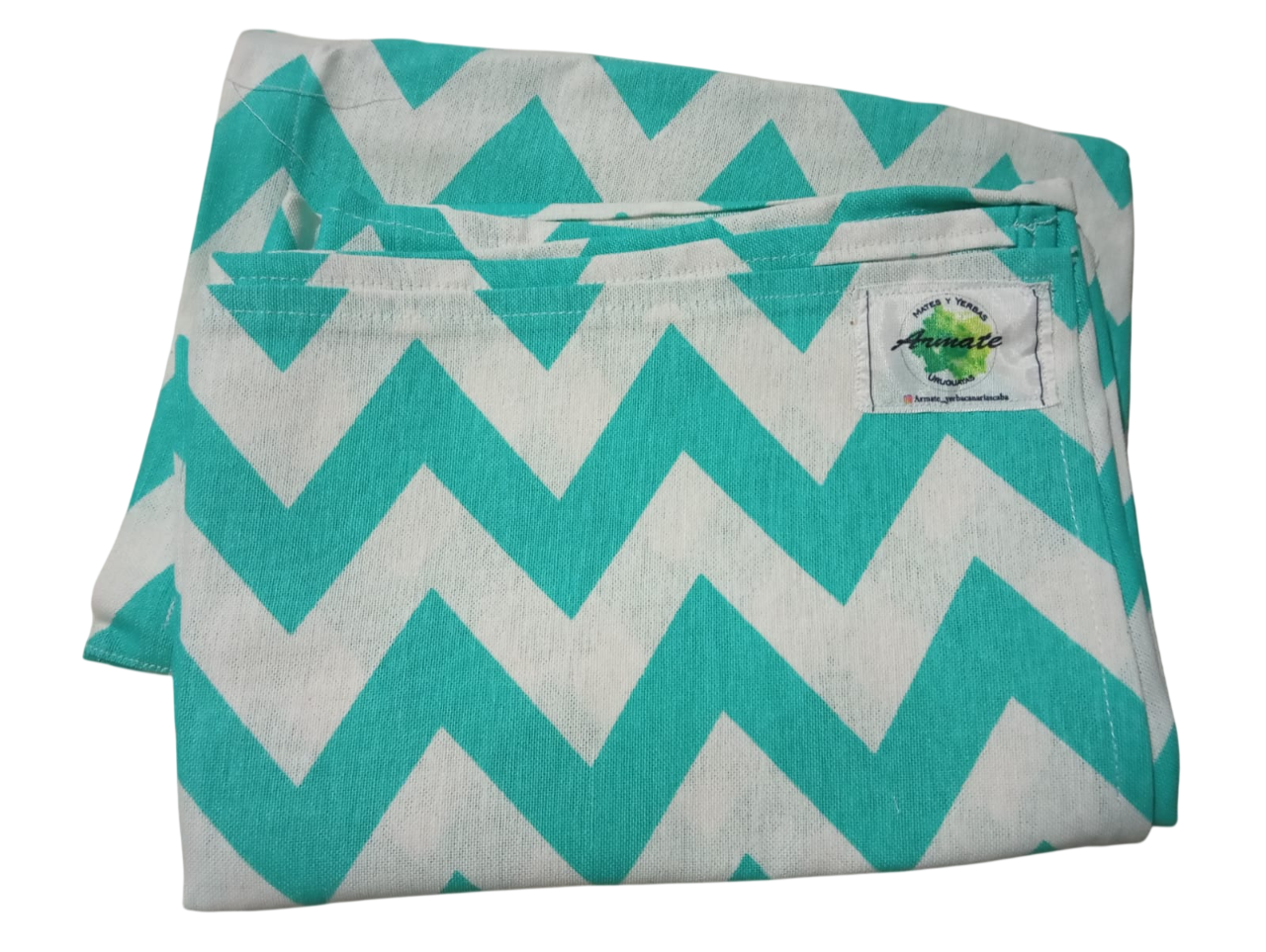 Manta con estampado de chevrones en verde azulado y blanco, doblada. Etiqueta blanca en la esquina superior derecha.