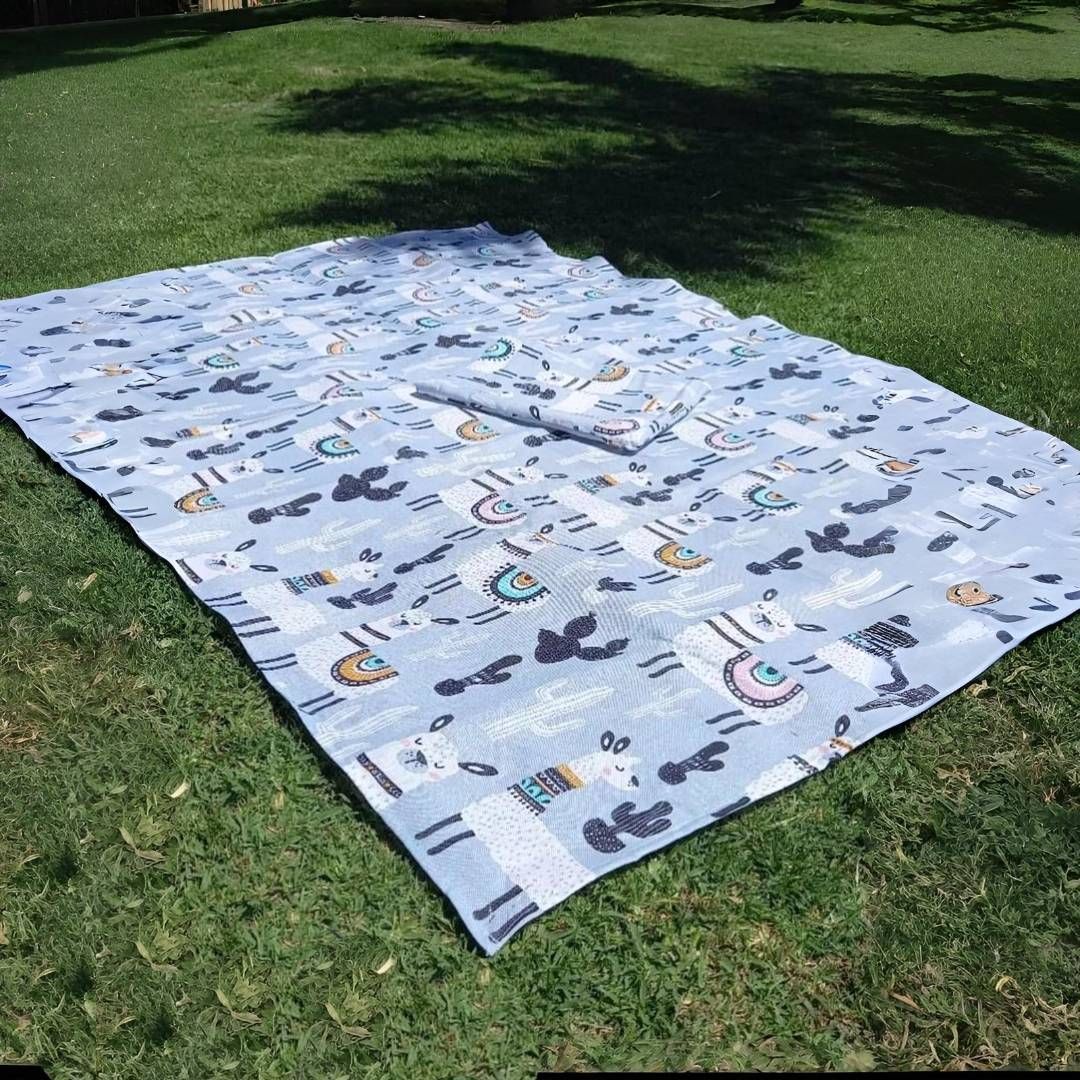 Manta de picnic con estampado de llama azul sobre césped verde al aire libre, parcialmente enrollada.