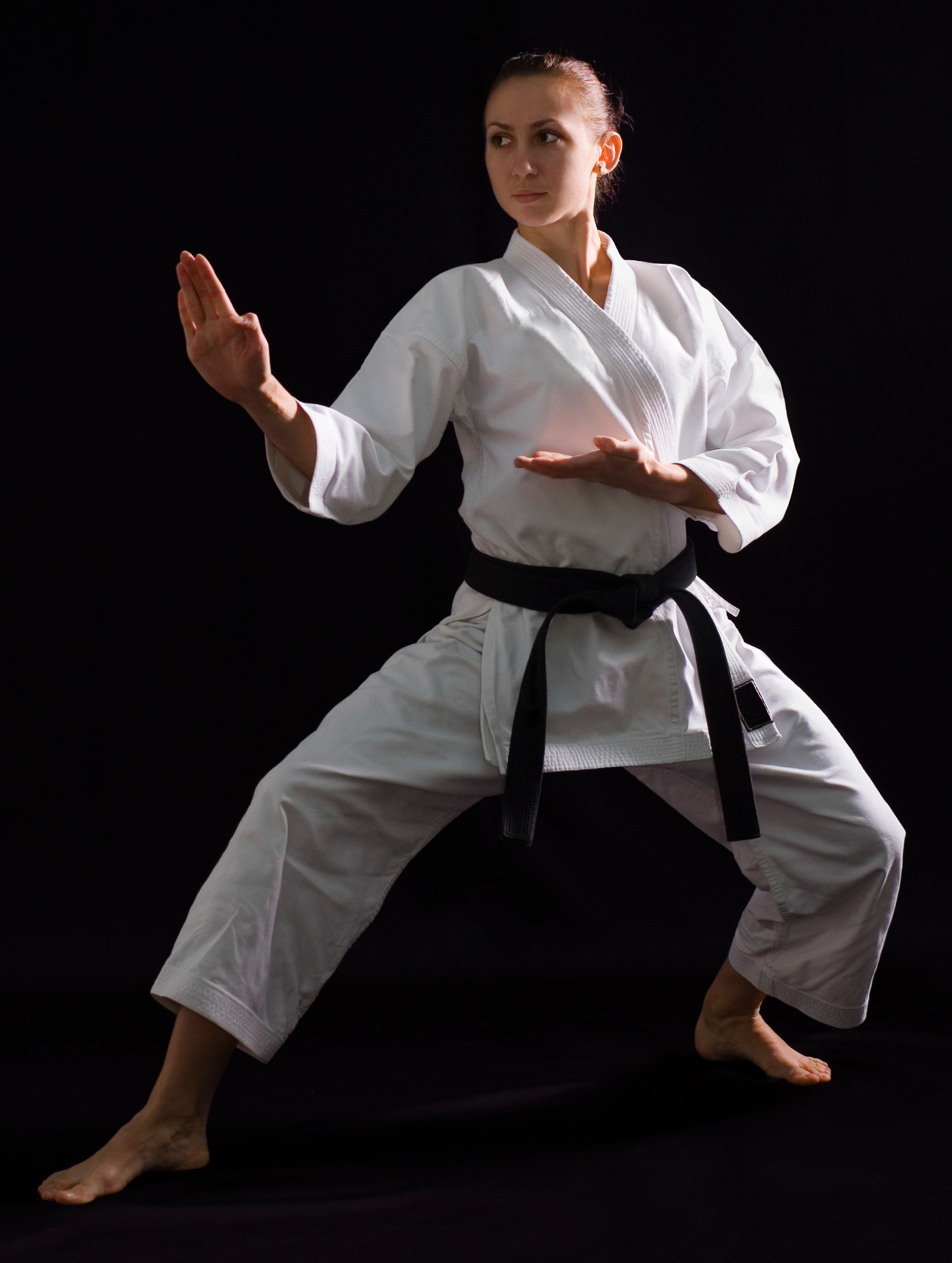 A woman in a white karate uniform with a black belt is practicing karate.