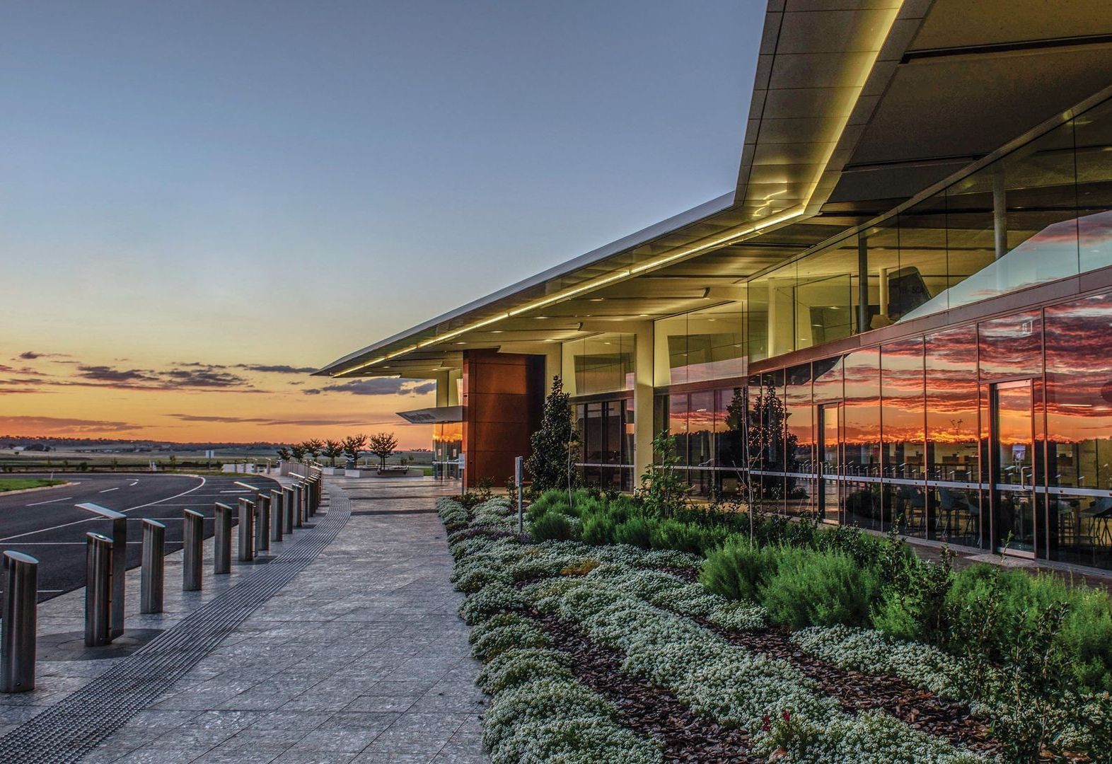 A large building at an airport with a lot of windows and a sunset in the background.
