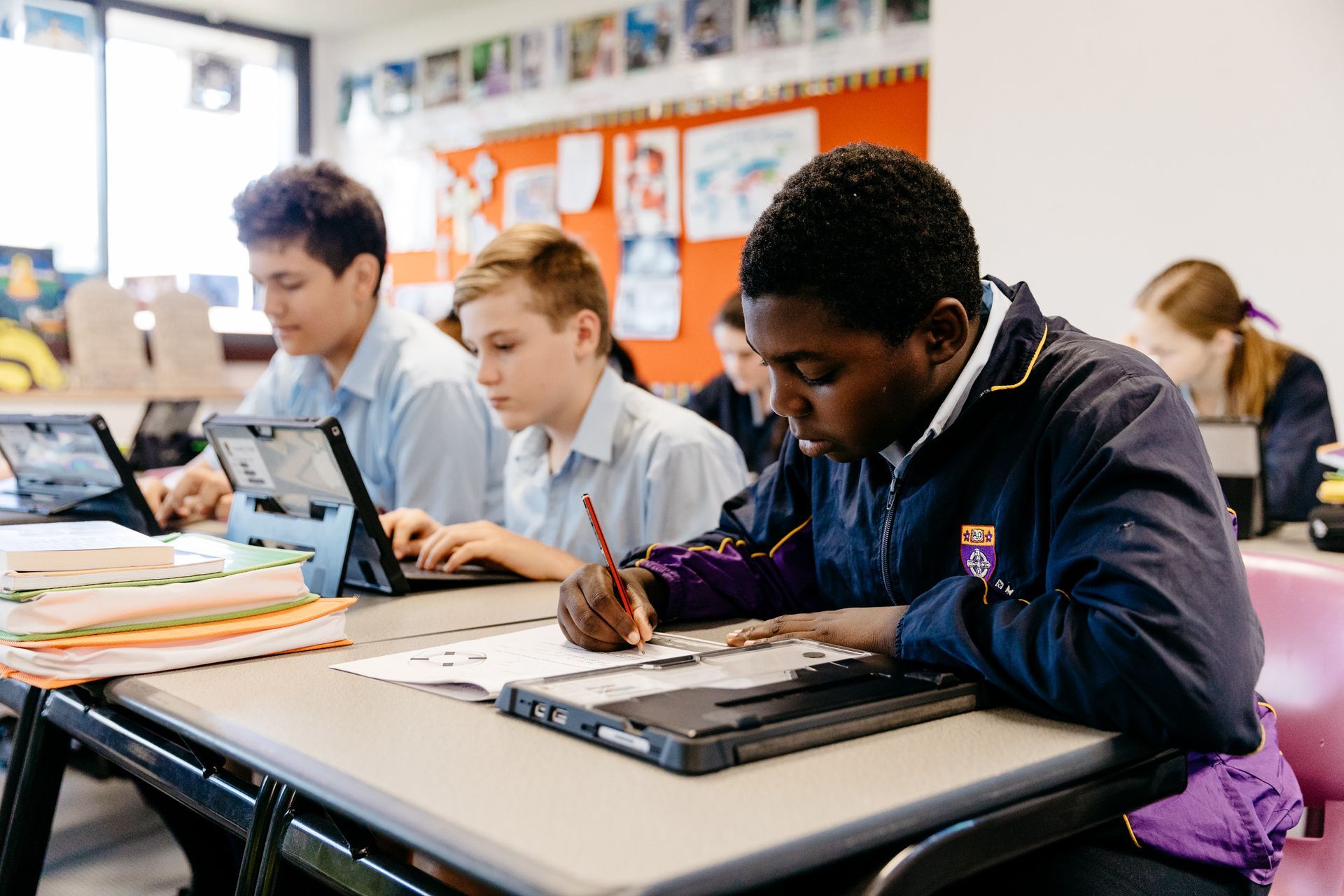 A group of children are sitting at desks in a classroom using laptops.