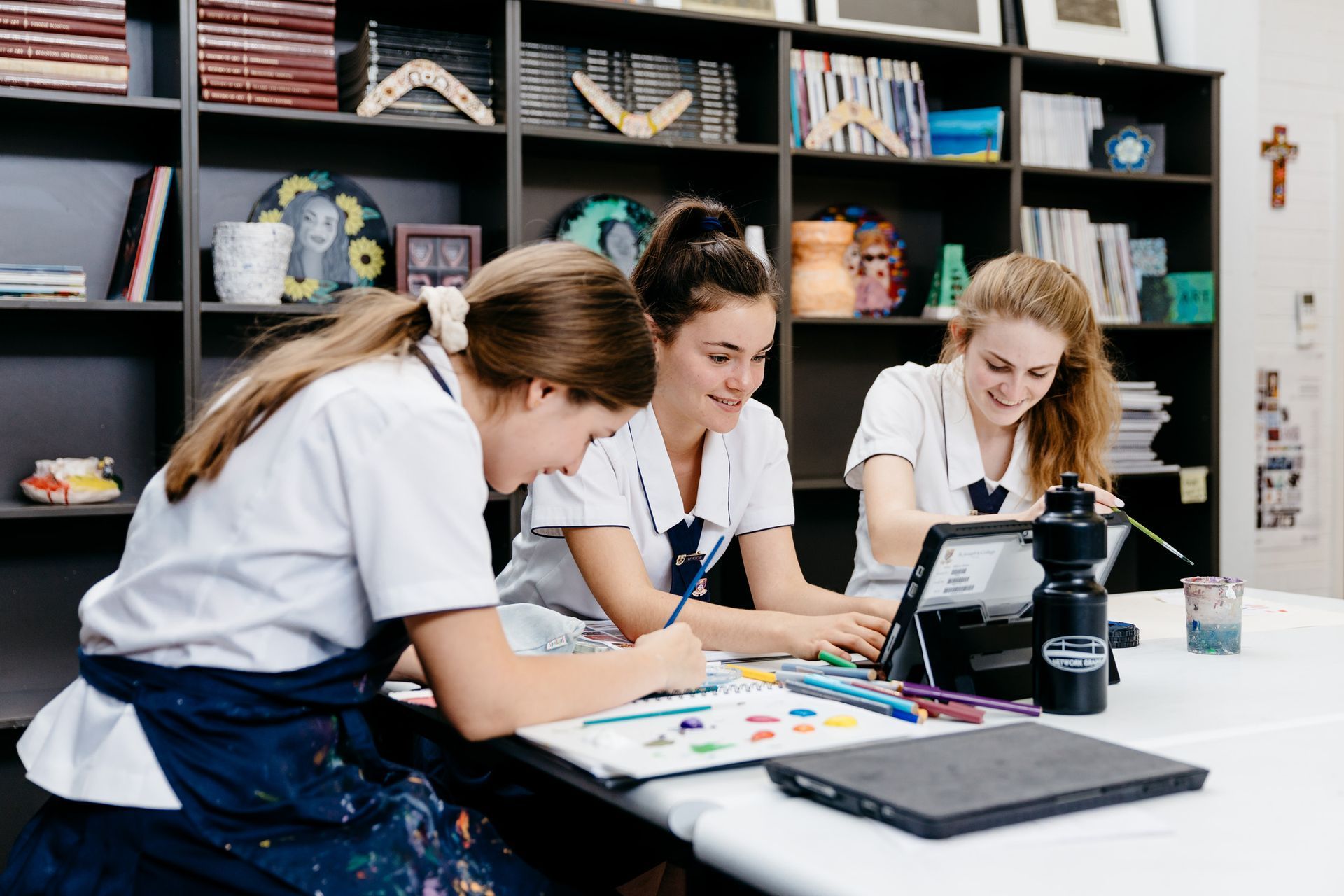 Three girls are sitting at a table looking at a tablet.
