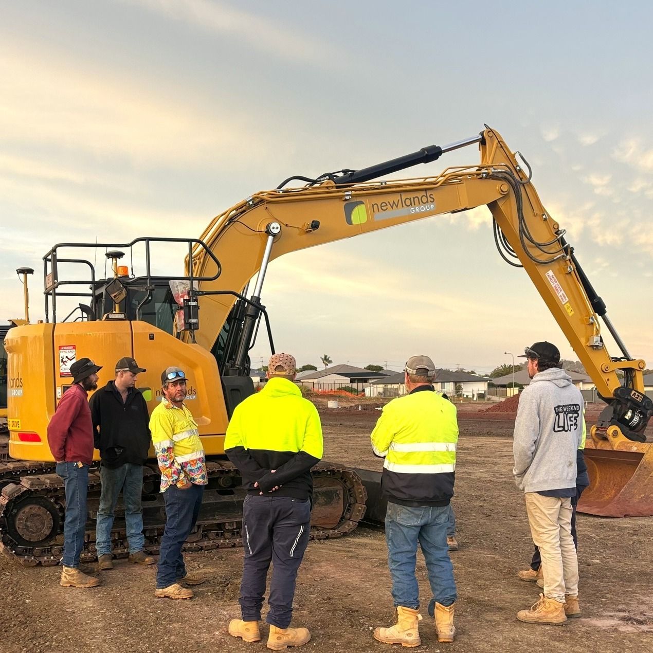 A group of construction workers are standing in front of a large yellow excavator.