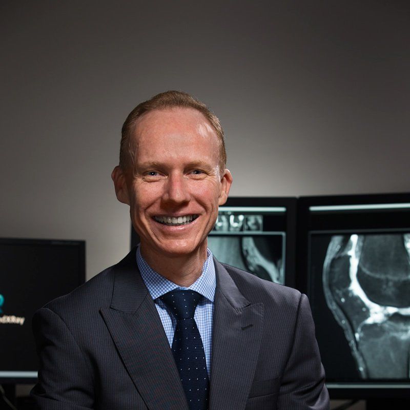A man in a suit and tie is smiling in front of x-rays