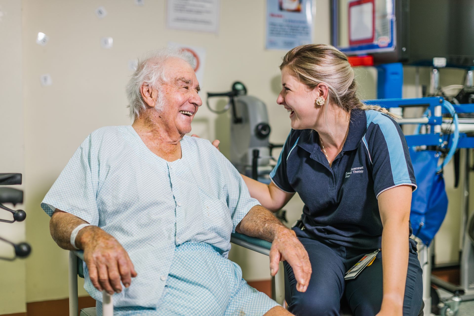 A nurse is talking to an elderly man in a hospital bed.