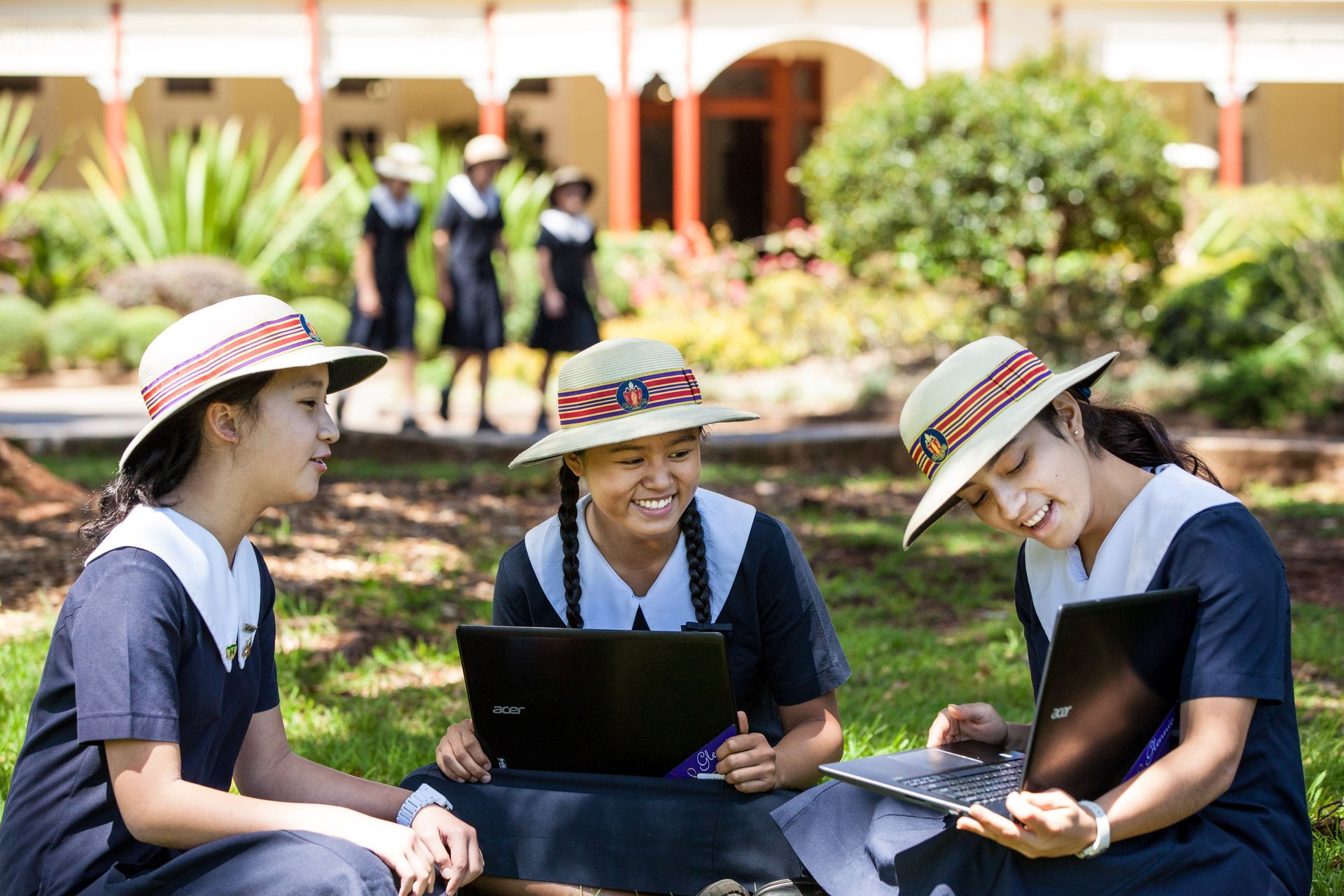 Three girls are sitting on the grass looking at a laptop.