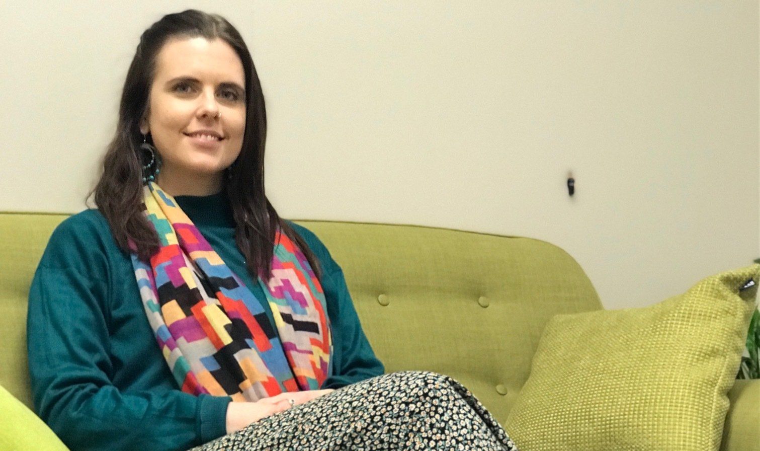 A woman is sitting on a green couch wearing a scarf.
