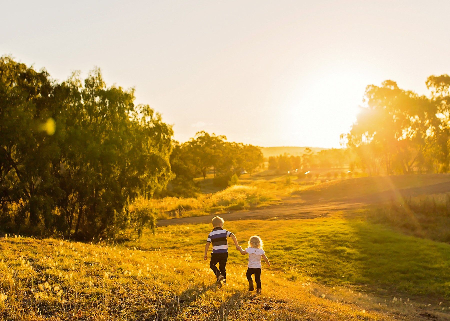 A boy and a girl are running through a field at sunset.