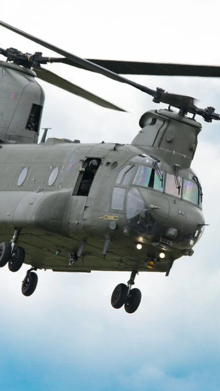 A military helicopter is flying through a cloudy sky