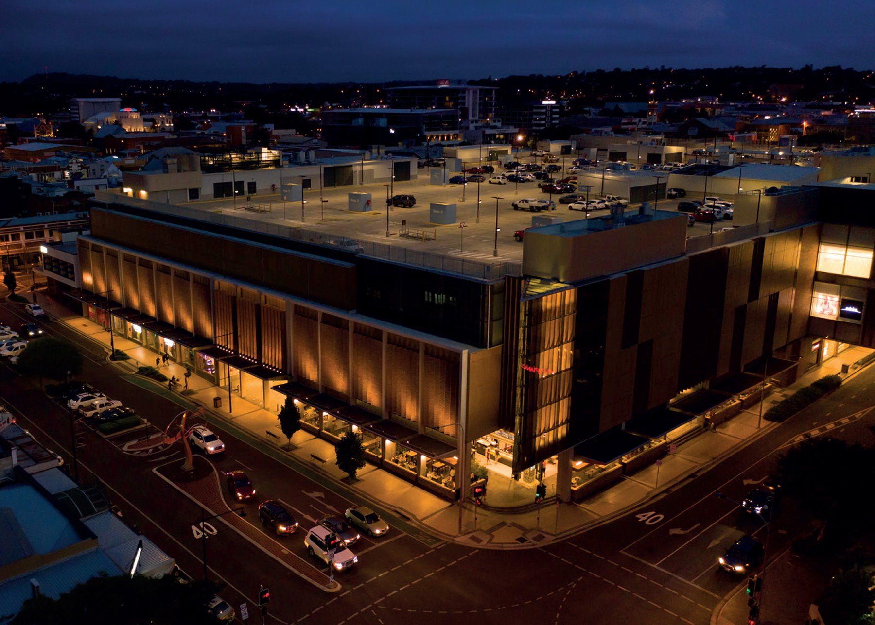 An aerial view of a parking garage at night with cars parked in front of it.