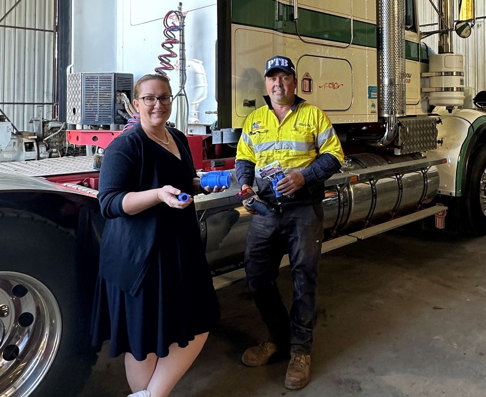 A man and a woman are standing next to a truck in a garage.