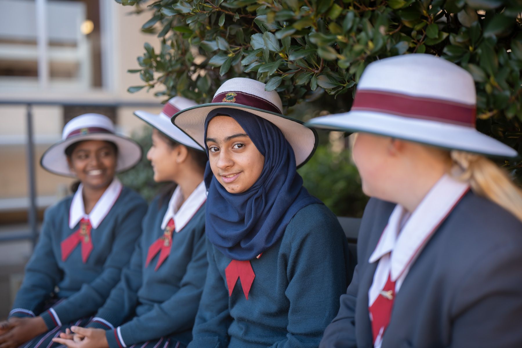 A group of girls in school uniforms and hats are sitting on a bench.