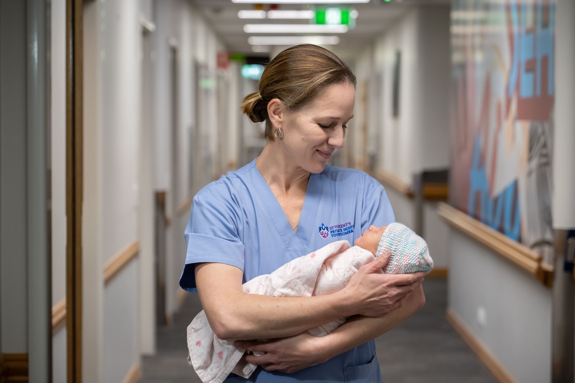 A nurse is holding a newborn baby in a hospital hallway.
