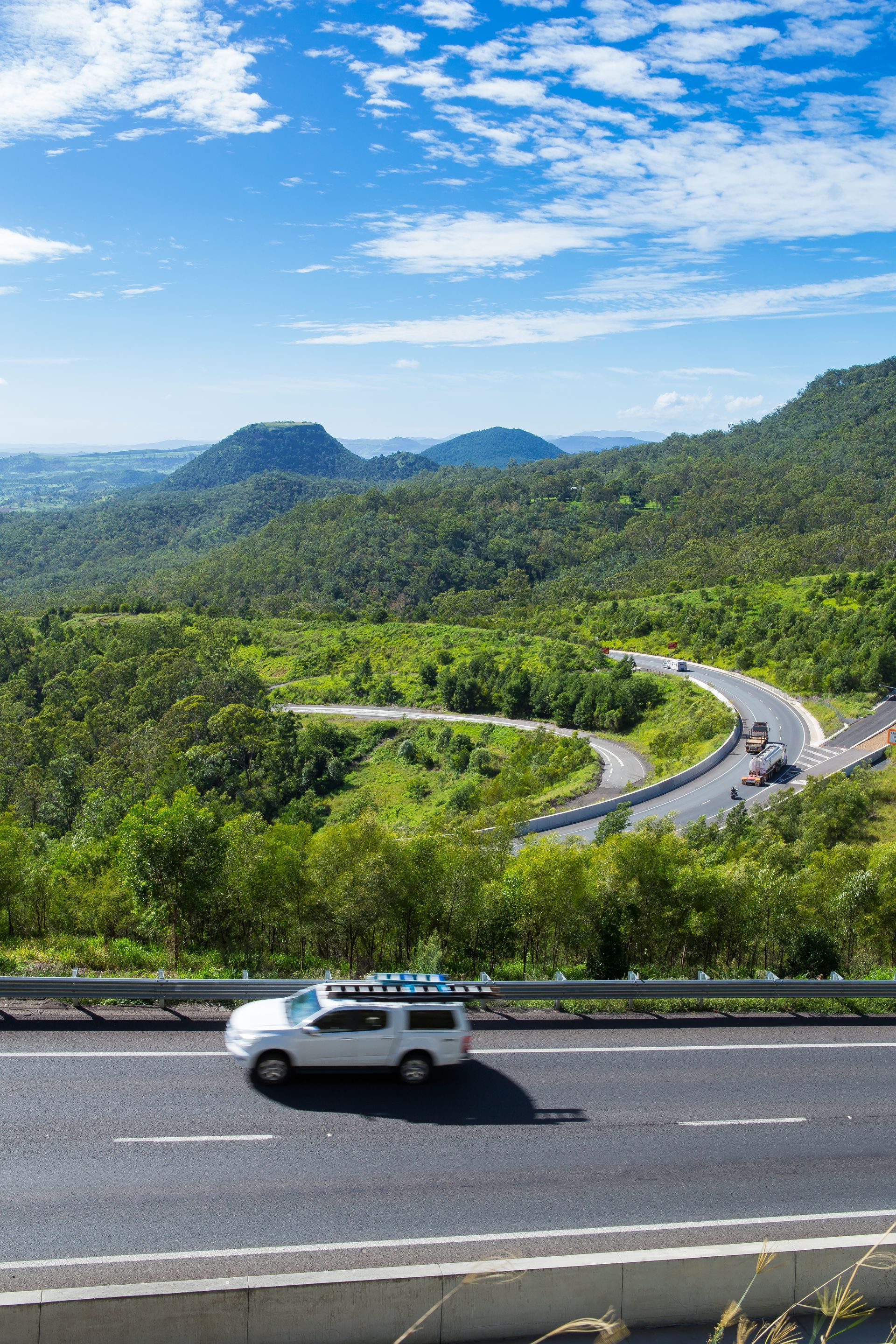 A white van is driving down a highway with mountains in the background.