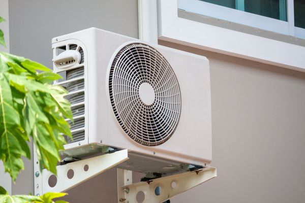 A white air conditioner is mounted on the side of a building next to a window.