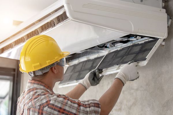 A man wearing a hard hat and gloves is working on an air conditioner.