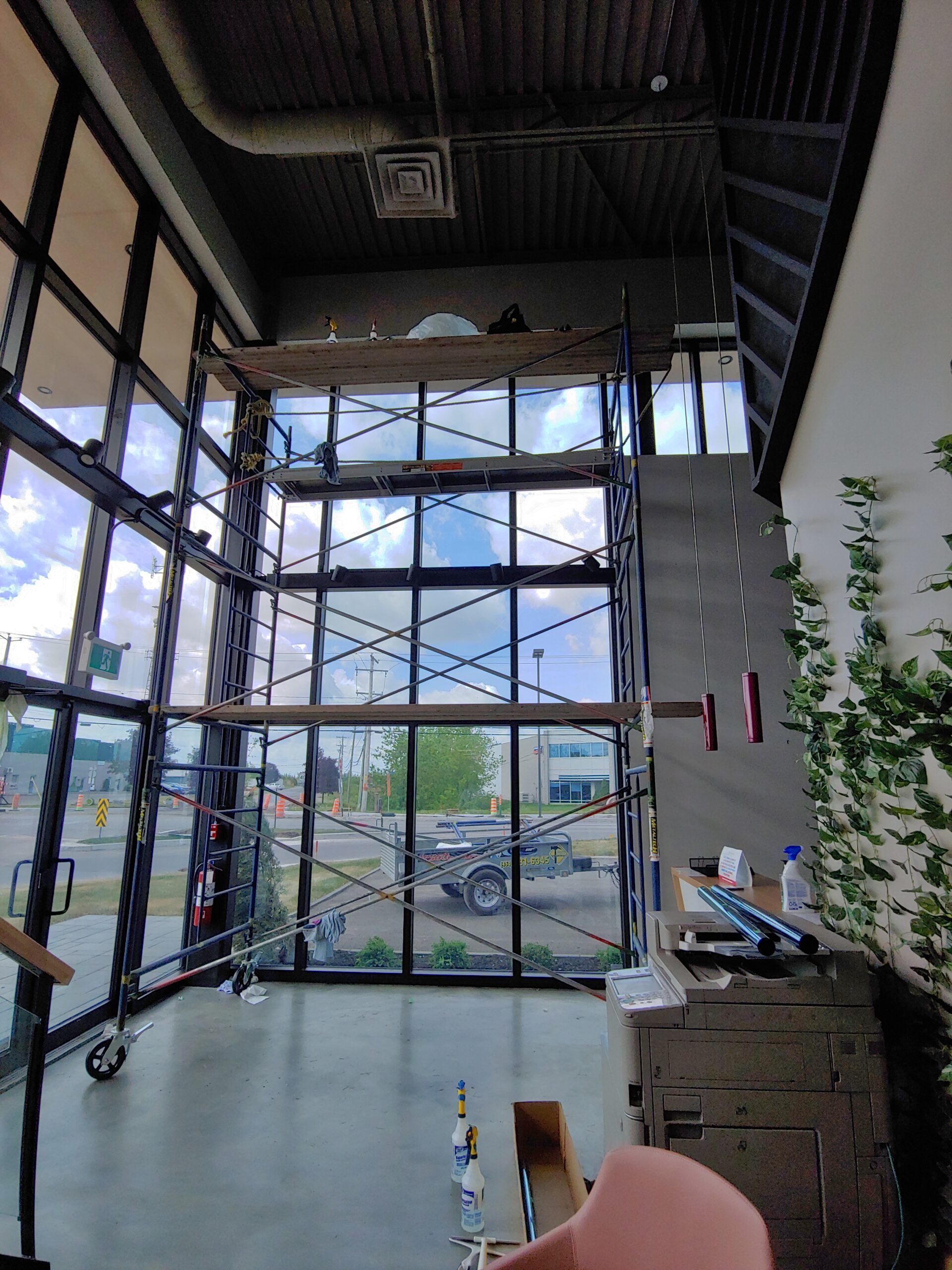 Vue intérieure d'un bâtiment avec des échafaudages devant de grandes fenêtres, dévoilant une rue et des travaux de construction en cours.