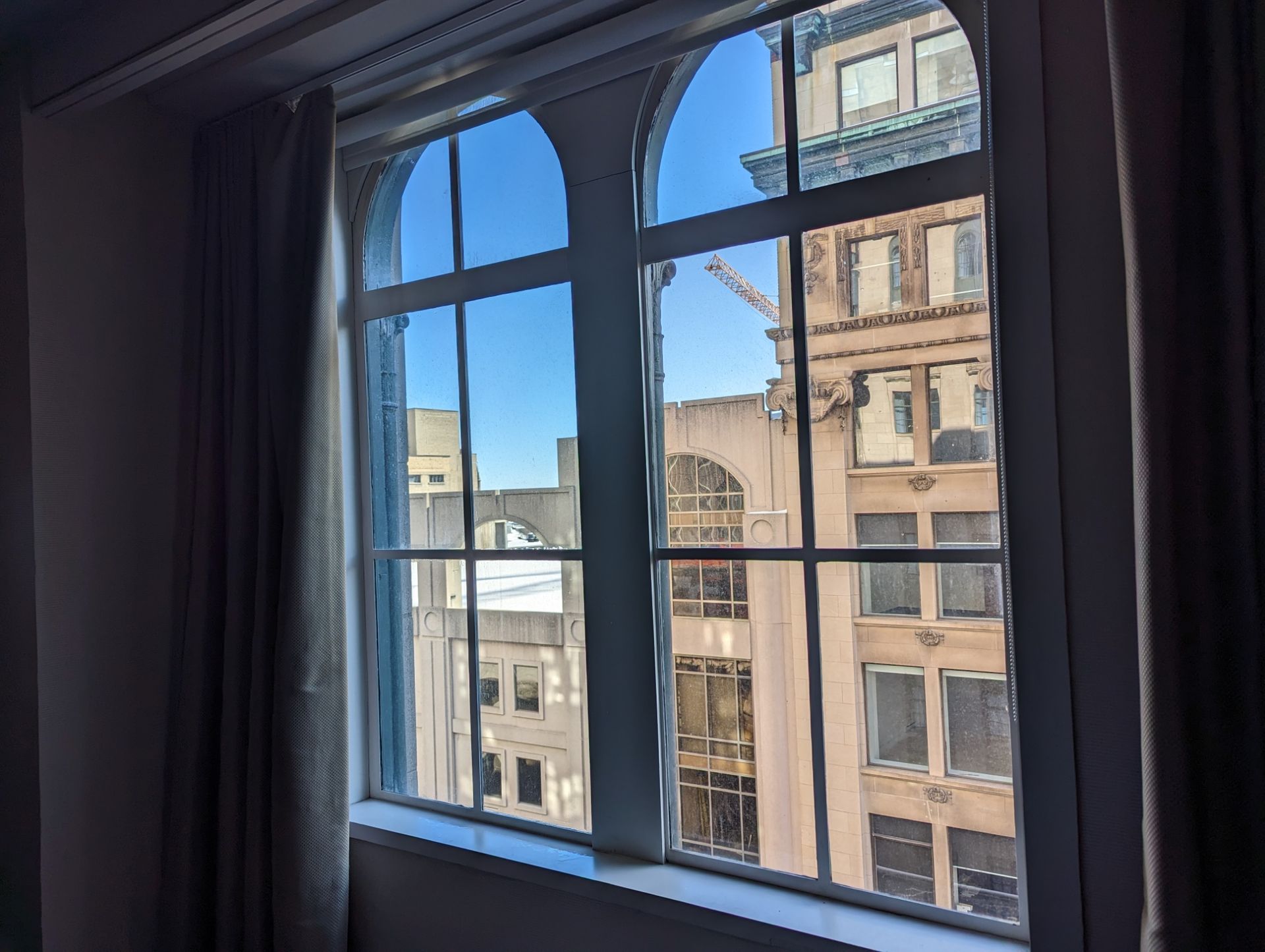 Vue du paysage urbain depuis la fenêtre : fenêtres cintrées, ciel bleu, vieux bâtiments, façades beiges et brunes.