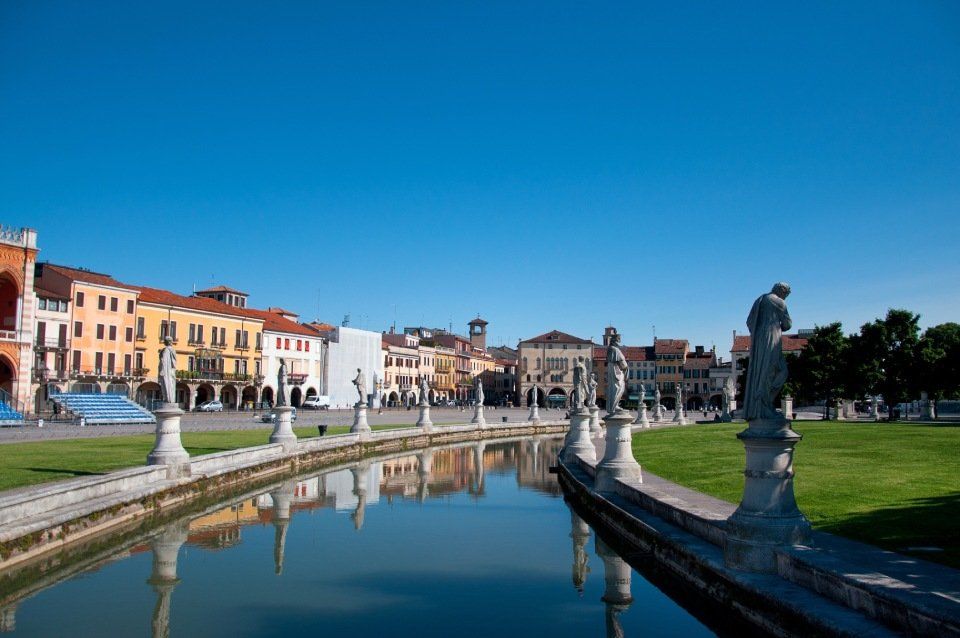 Statue di Prato della Valle a Padova, in Italia, che conduce a una piazza con edifici colorati sotto un cielo azzurro.