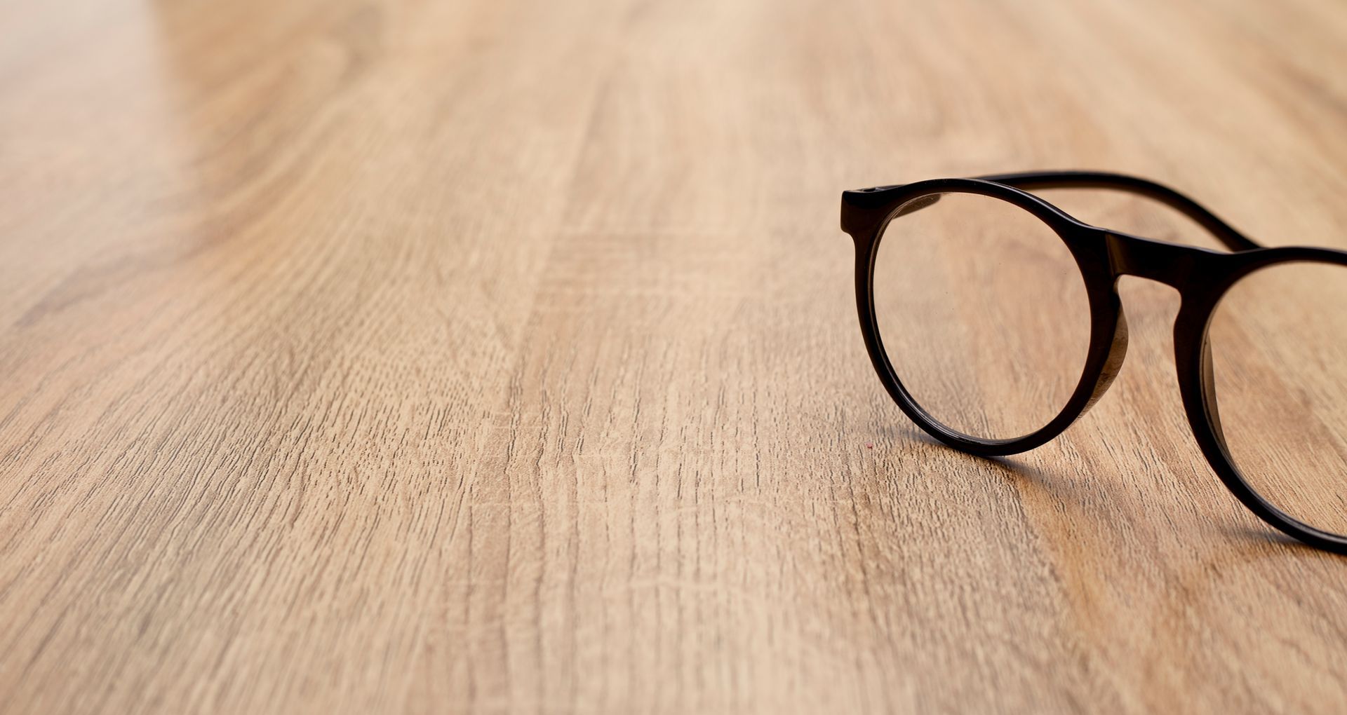 A pair of glasses is sitting on a wooden table.