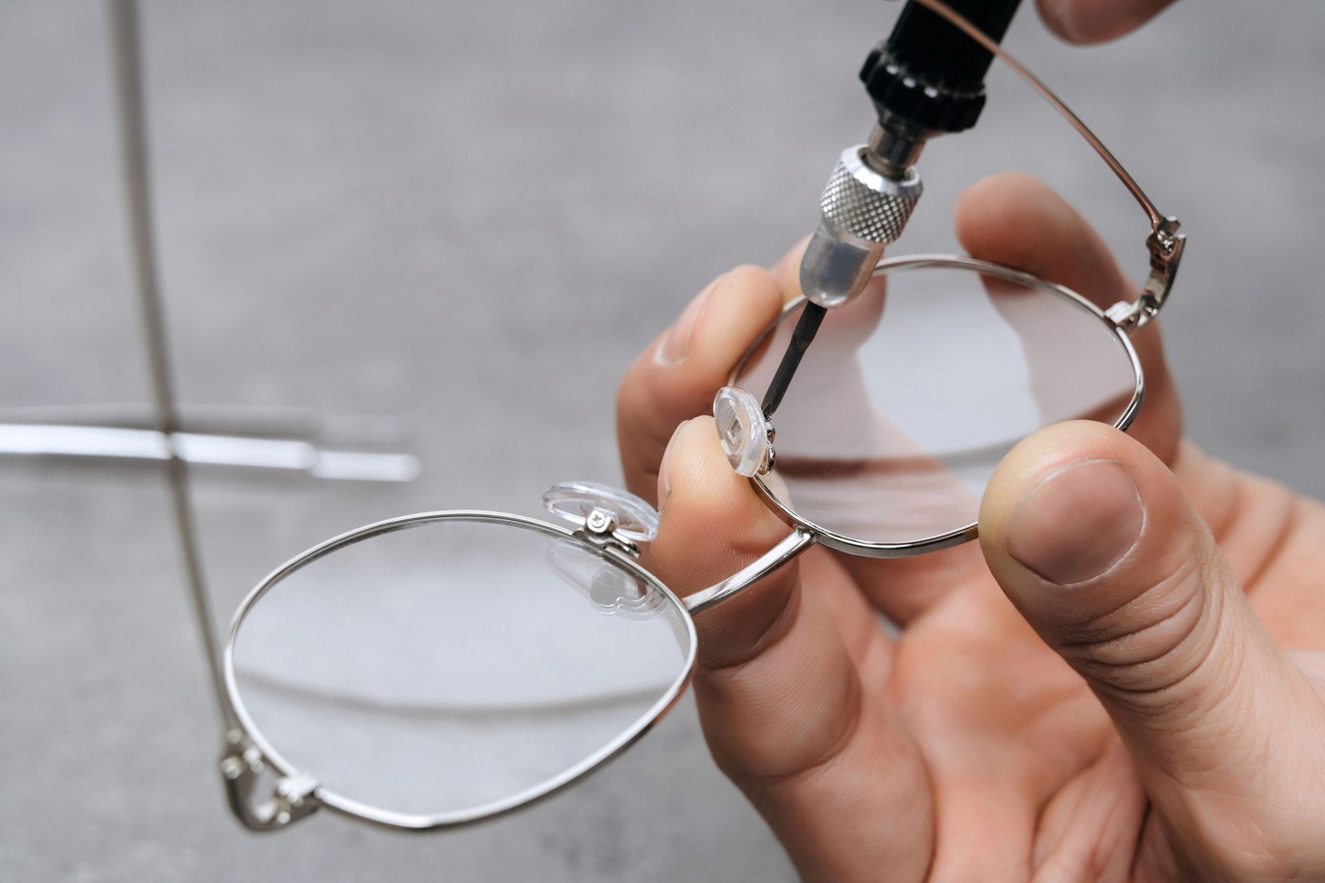 A person is fixing a pair of glasses with a screwdriver