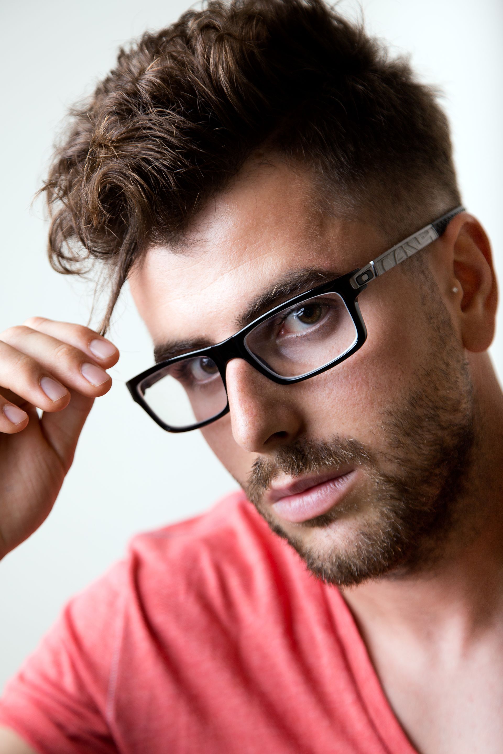 A man wearing glasses and a red shirt is touching his hair.