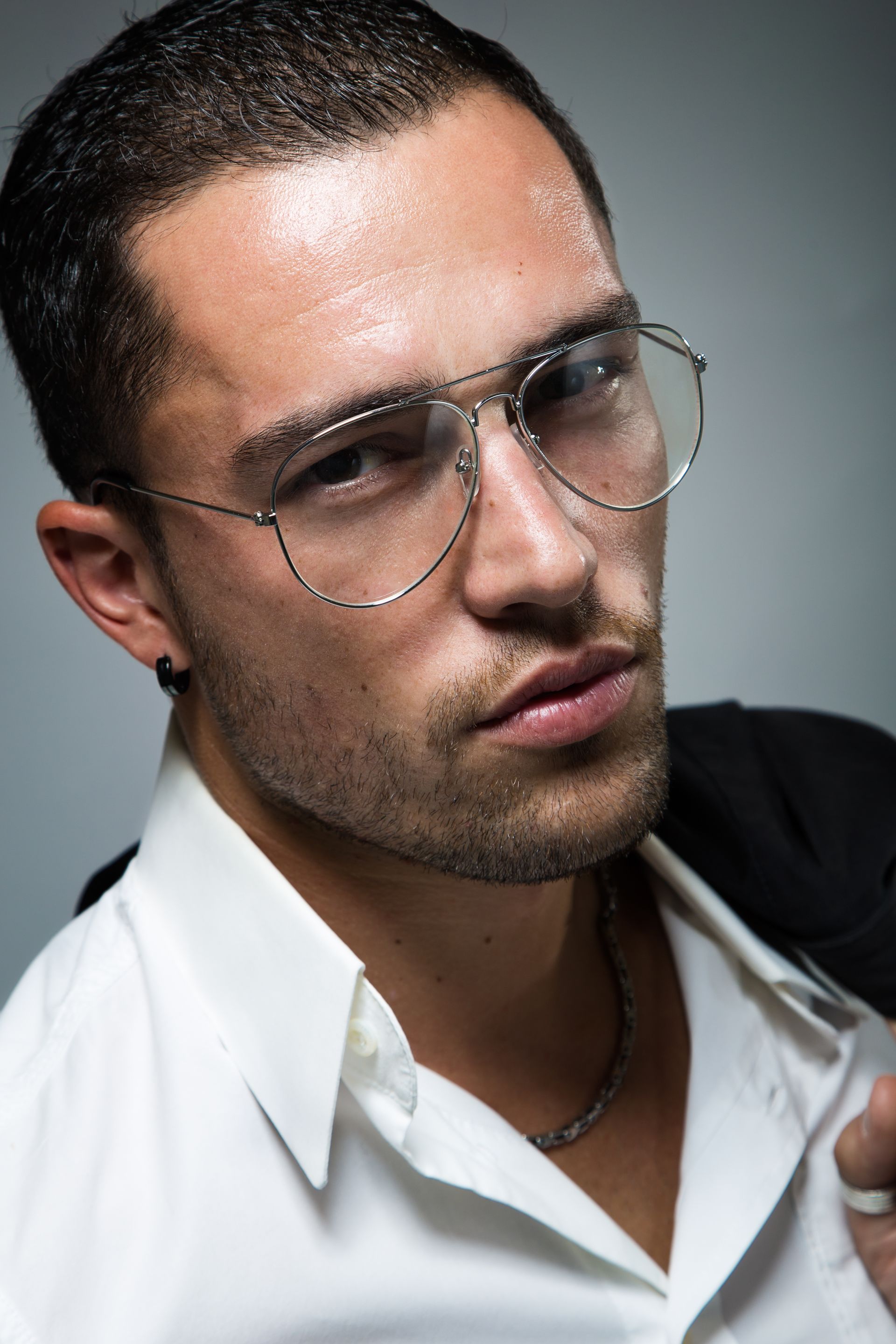 A man wearing glasses and a white shirt is holding his jacket over his shoulder.