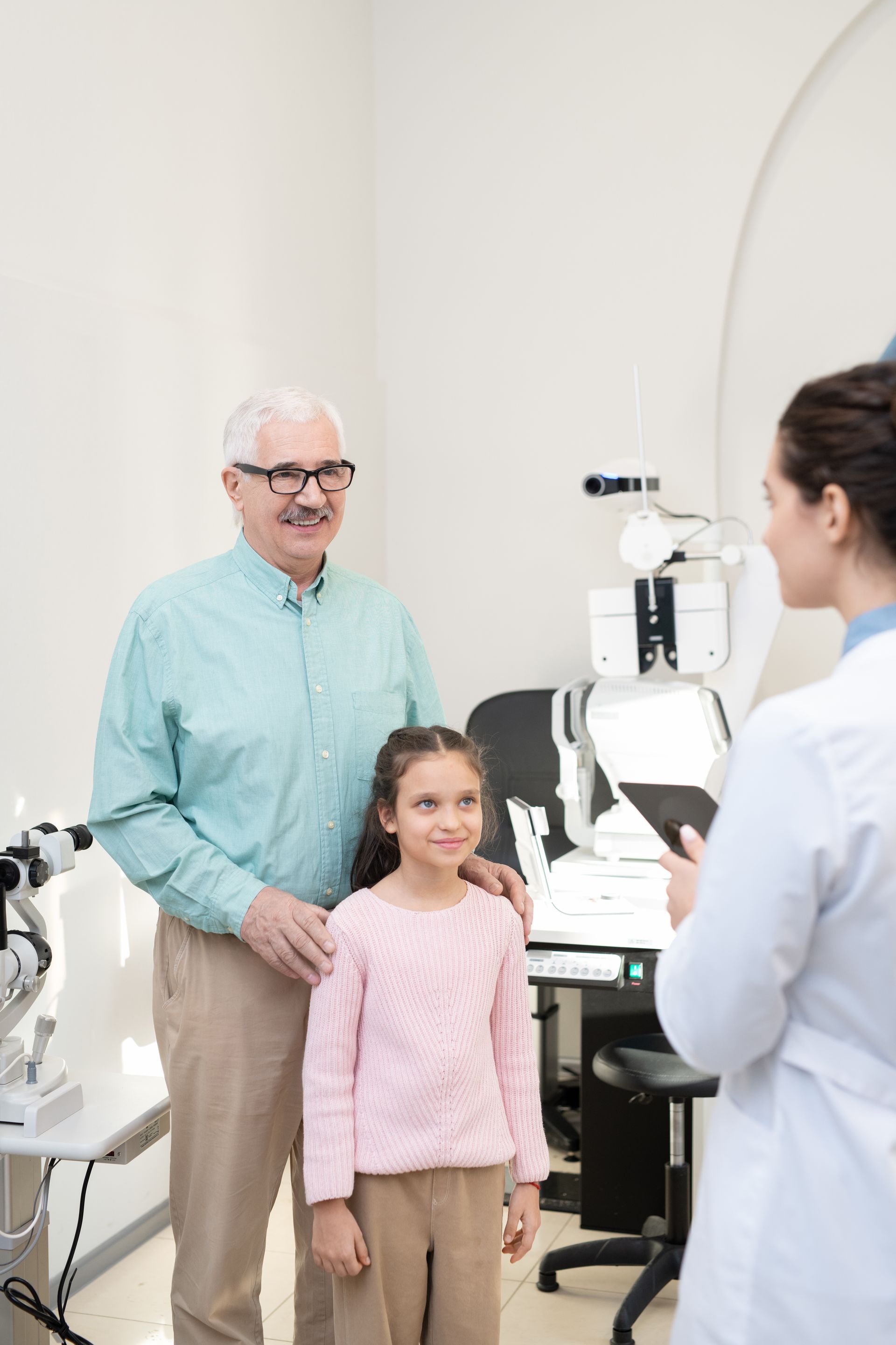 An elderly man and a little girl are standing next to each other in an ophthalmologist 's office.